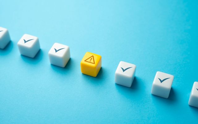 青の背景の前にあるいくつかのチェックマークのブロックと1つの注意マークのブロック