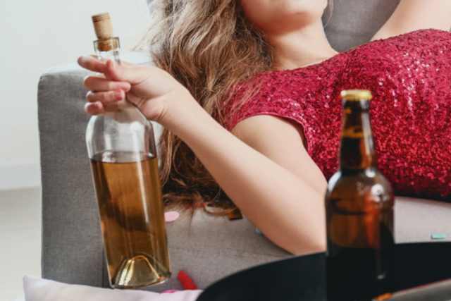 お酒のボトルをもちながらソファに寝転んでいる女性