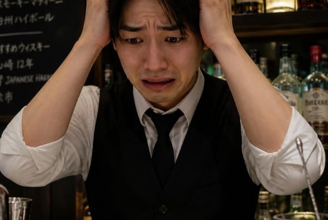 「しくじった」という顔をしているバーテンダーの服装をした若い日本人男性