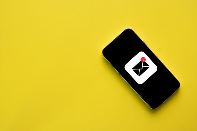 黄色い背景の前にあるメールマークが出た携帯