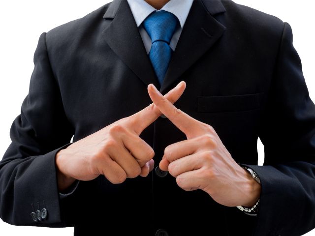 両手の人差し指でばつ印を作るスーツ姿の男性