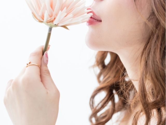 薄ピンクの花に唇を寄せる女性