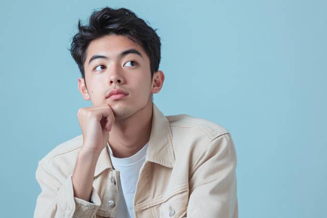 青い背景の前で何かを考える男性