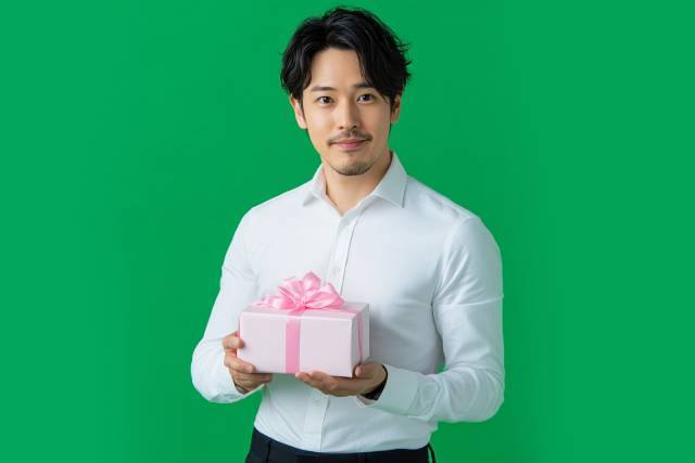 ピンクのリボンがついたプレゼントを持つスーツの男性