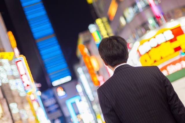 東京の繁華街に立つ後ろ姿のスーツを着た男性