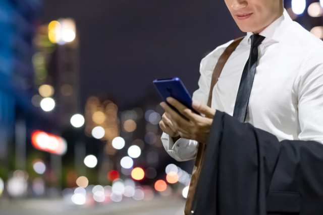 夜の街でスマホをいじるビジネスマン