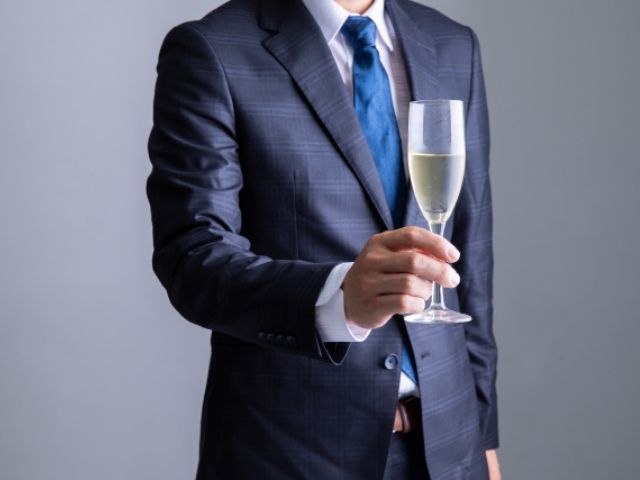 紺色のスーツを着て、白ワインを片手に持つ男性