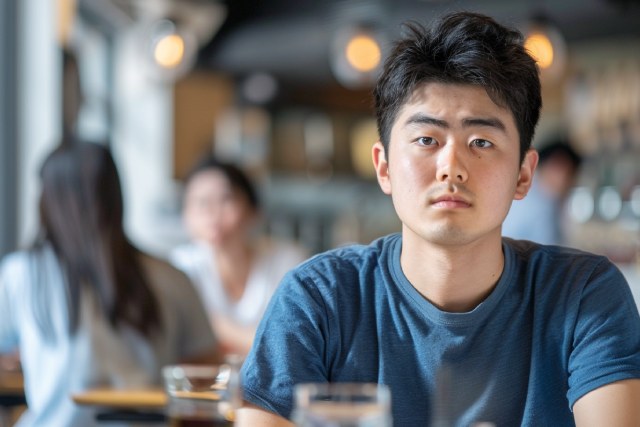 昼間のカフェの店内で座っている無表情の日本人男性