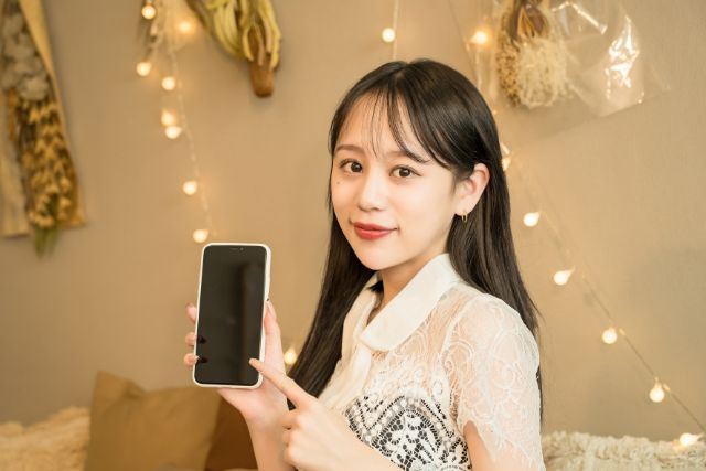 白いドレスを着てスマートホンを右手にもつロングヘアの女性