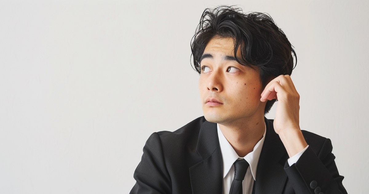 右ななめ上を見つめる黒いスーツを着ている日本人の若い男性