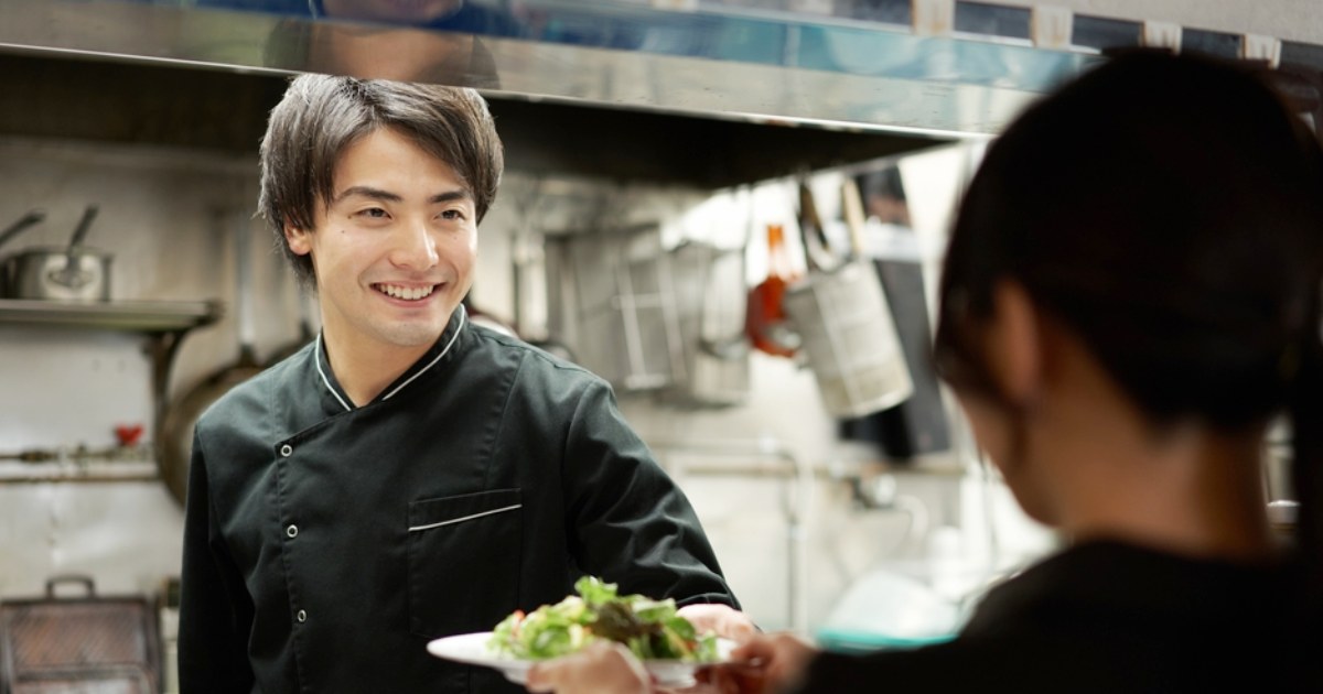 スタッフに料理のサラダを渡す若い男性料理人