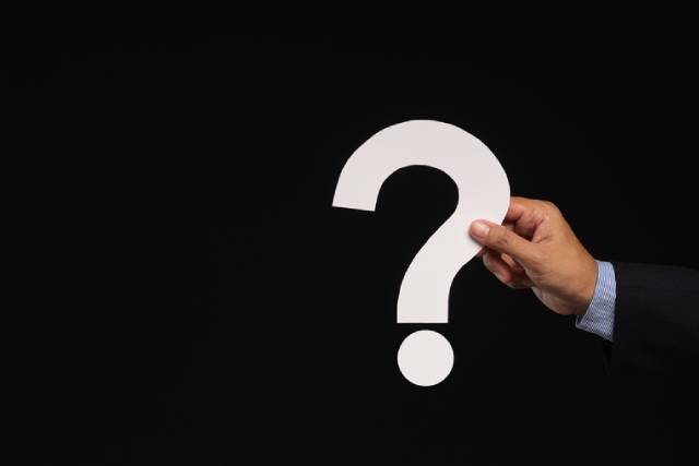 黒いスーツを着た男性がクエスチョンマークをもっている手元