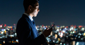 夜の屋上で携帯を触るスーツの男性