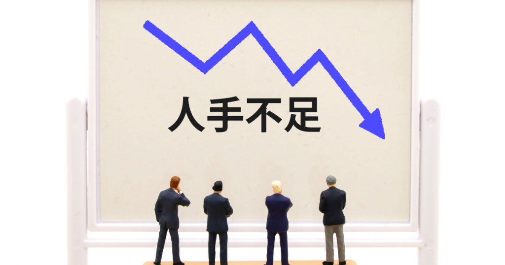 ホワイトボードに書かれた人手不足の文字とスーツ姿の男性ミニチュア