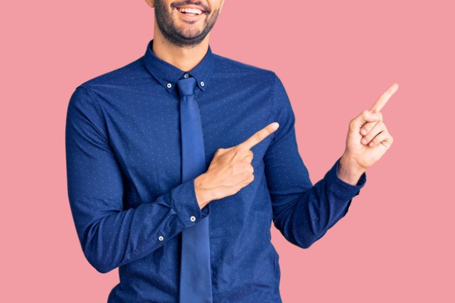 ピンクの背景に立つ青いシャツと青いネクタイの指を指している男性