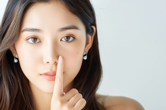 口元に人差し指をつけて秘密のポーズをしている若い女性