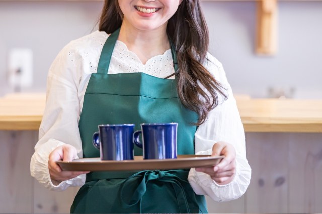 青いコップをお盆に載せて笑顔で運ぶカフェの女性店員