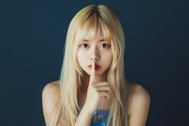 黒い背景で口に人差し指をあてている金髪の女性