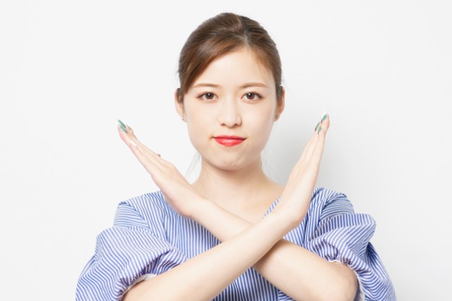 20代後半の日本人の女性が腕をクロスしてバツマークを作っている様子