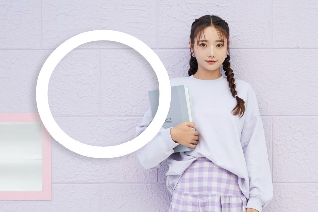 ラベンダー色の壁にもたれかかって立っている三つ編みヘアの女子大生と丸マーク