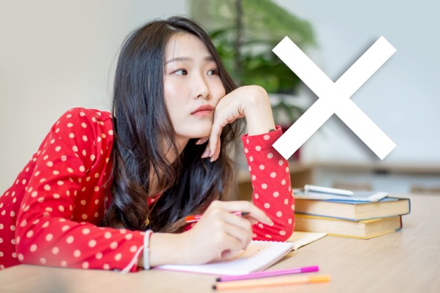 だるそうな表情で講義を聞く赤い服の女子大生とバツマーク