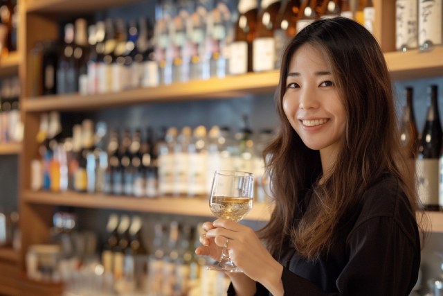 ワイングラスを持った30代の日本人女性が笑顔でこちらを向いている
