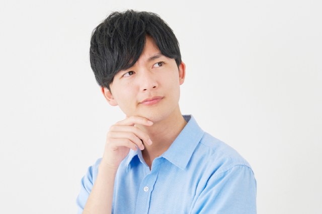 水色の服を着た若い日本人男性が考え事をしている様子