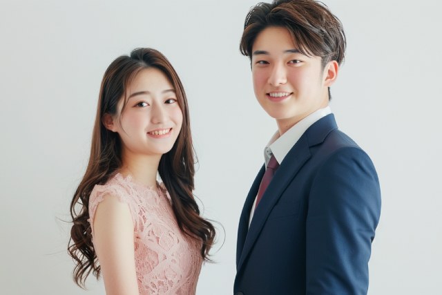 ピンク色のドレスを着た若い女性とネイビーのスーツを着た若い男性が笑顔でこちらを見ている様子
