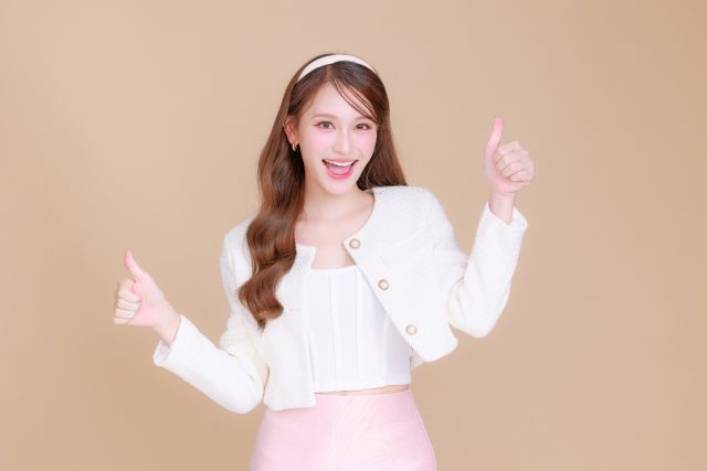 茶色の背景にグッドサインをしているロングヘアの女性