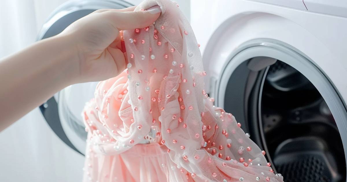 ビジューがついたピンクのチュールドレスを洗濯機にいれようとしている女性の手元のクローズアップ
