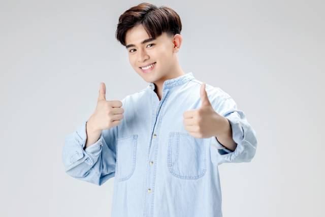 両手の親指を立てた七三分けの髪型をした男性