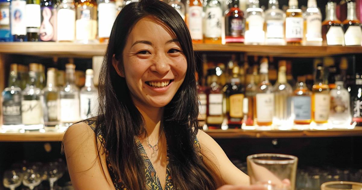 バーカウンターにたち、お客さんにお酒が入ったグラスを差し出す笑顔の日本人女性