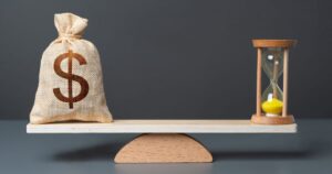 天秤にかけられたドル袋と砂時計