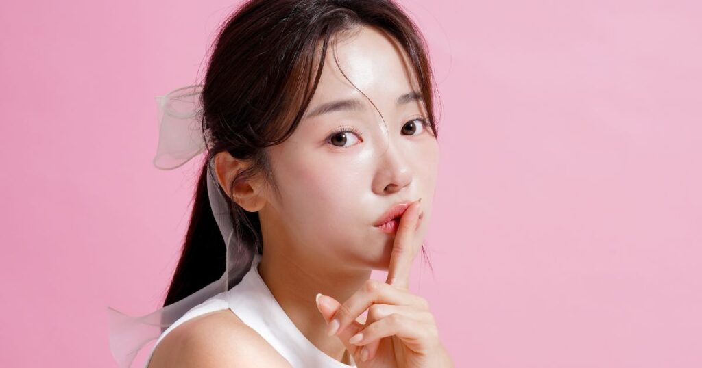 ピンクの壁の前で唇に人差し指を当てる若い女性