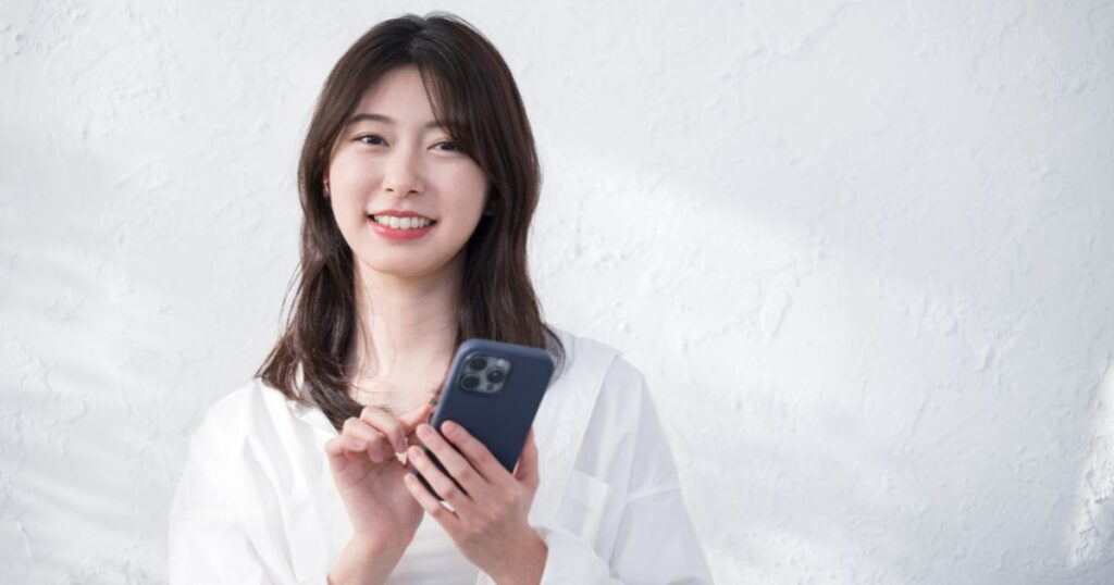 白いトップスを着た黒髪の清楚な女性がスマホを触っている様子