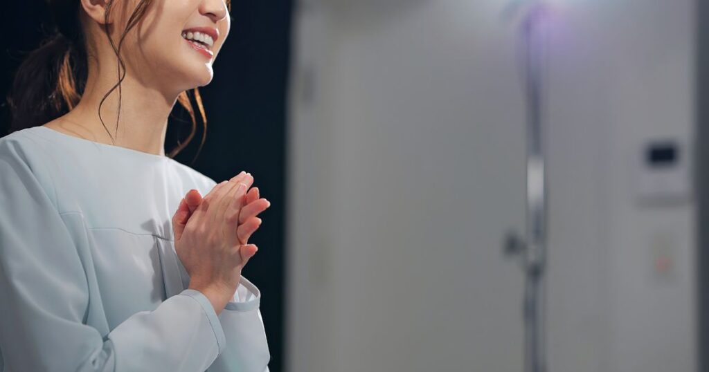 暗い部屋で照明を当てられて笑顔で手を合わせて話している様子の口元