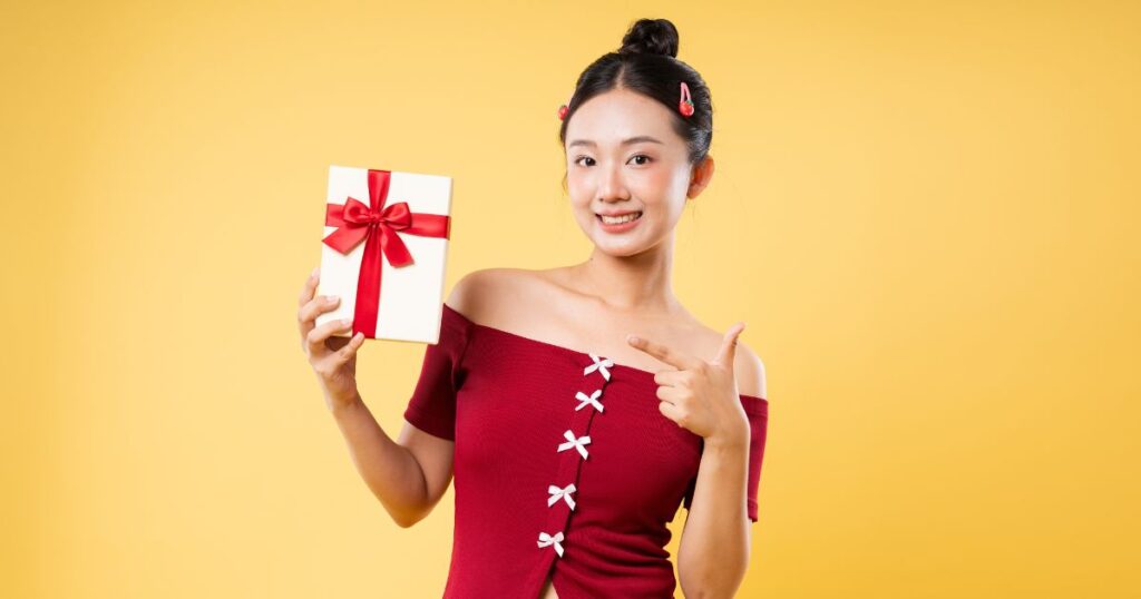 黄色い壁の前でプレゼントボックスを持って指差す若い女性