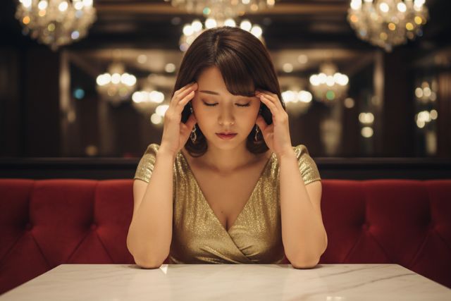 両手でこめかみに手を当てて俯いているゴールドのドレスを着たキャバ嬢