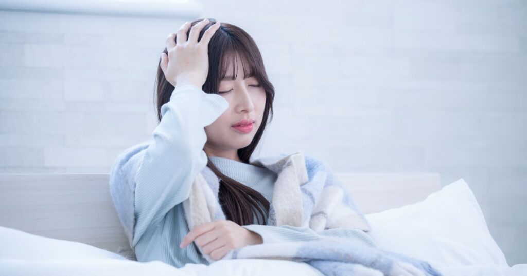 ベッドで頭をおさえる女性
