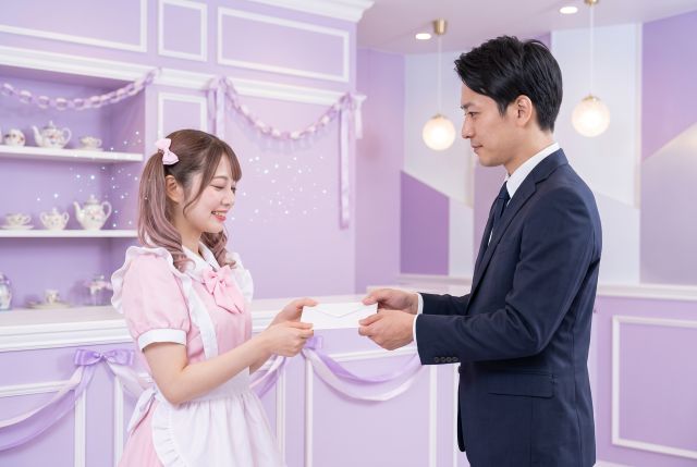 スーツの男性から給料をもらうメイド服の女性
