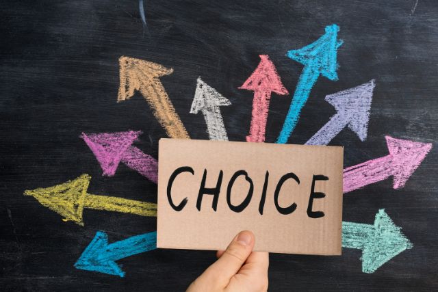 CHOICEと書かれたボードを持つ手と黒板に書かれたカラフルな矢印